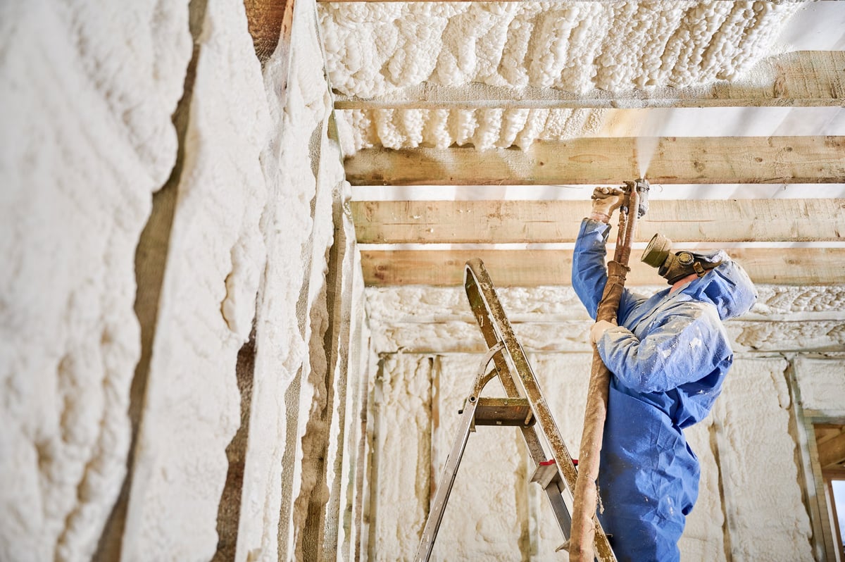 Contractor applying spray foam insulation to ceiling beams and wall cavities